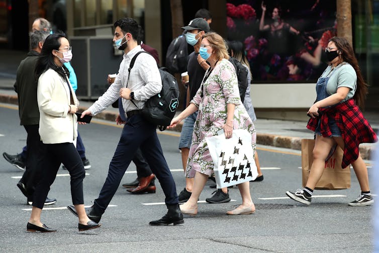 People wearing masks walking across street in Brisbane