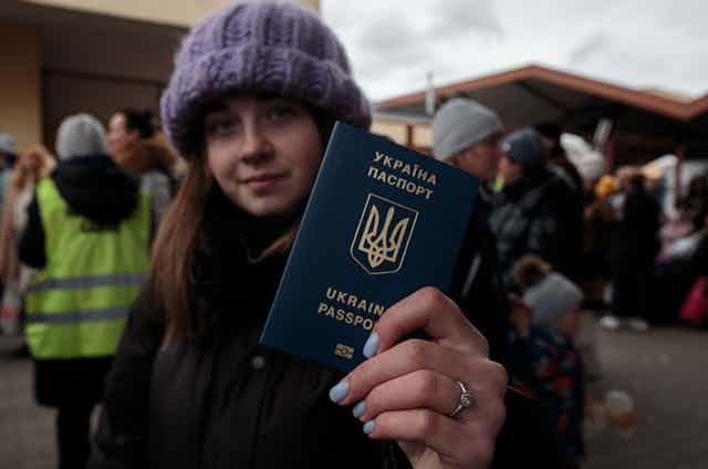 A young woman wearing a purple hat holds her Ukraine passport toward the camera