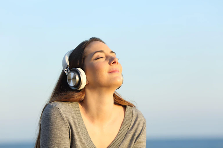 Woman sits outside in the sun wearing headphones.