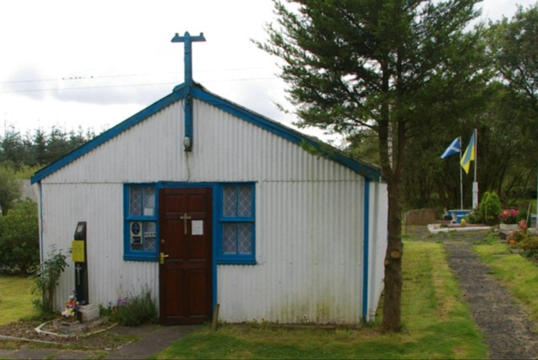 A corrugated iron roofed hut painted white with a green lawn surrounding it.