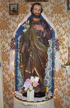 A wooden statue of St Joseph with a blue robe and flowers at his feet.