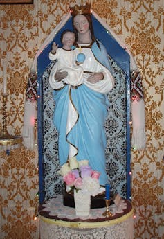 A statue of the Virgin Mary and child dressed in blue with flowers at her feet.
