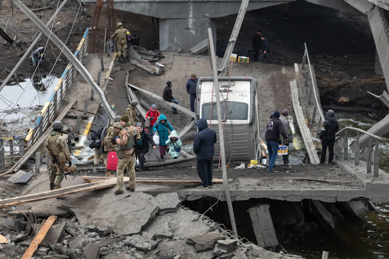 People crossing a makeshift bridge in Irpin, near Kyiv, as emergency workers watch.