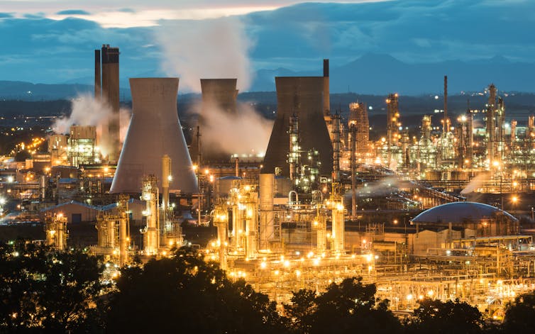 An industrial scene with three cooling towers and various chimneys lit up with yellow lights.