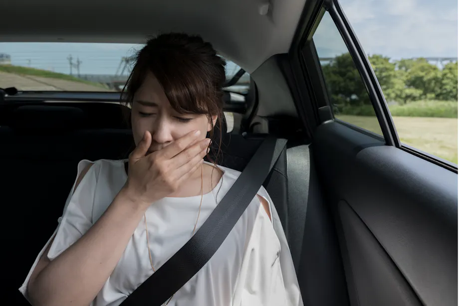 A woman in the backseat of a car covers her mouth due to feeling sick.