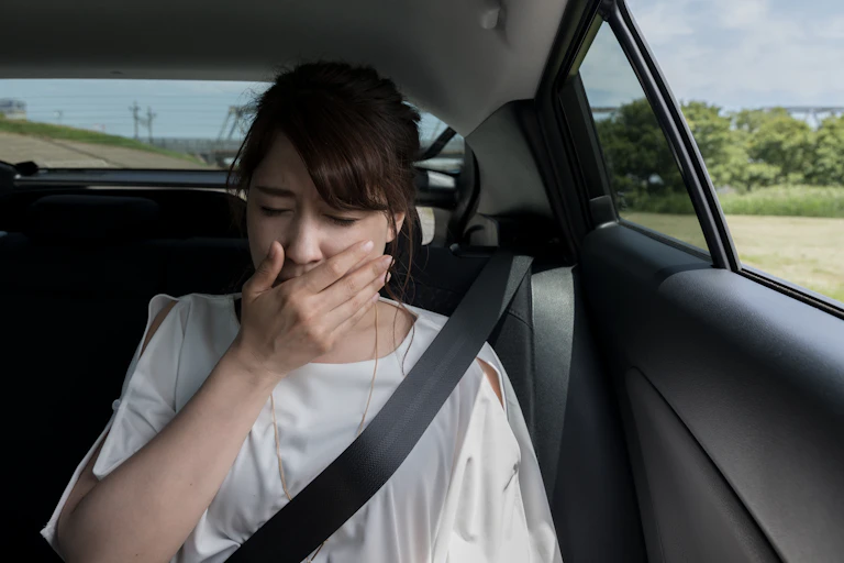 A woman in the backseat of a car covers her mouth due to feeling sick.