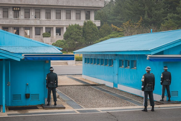 Two blue buildings with guards in uniform.
