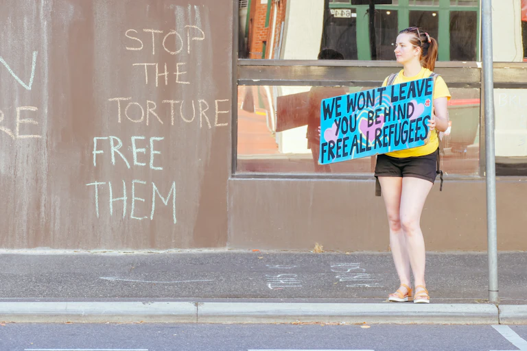 Woman with sign saying 'we won't leave you behind free all refugees'