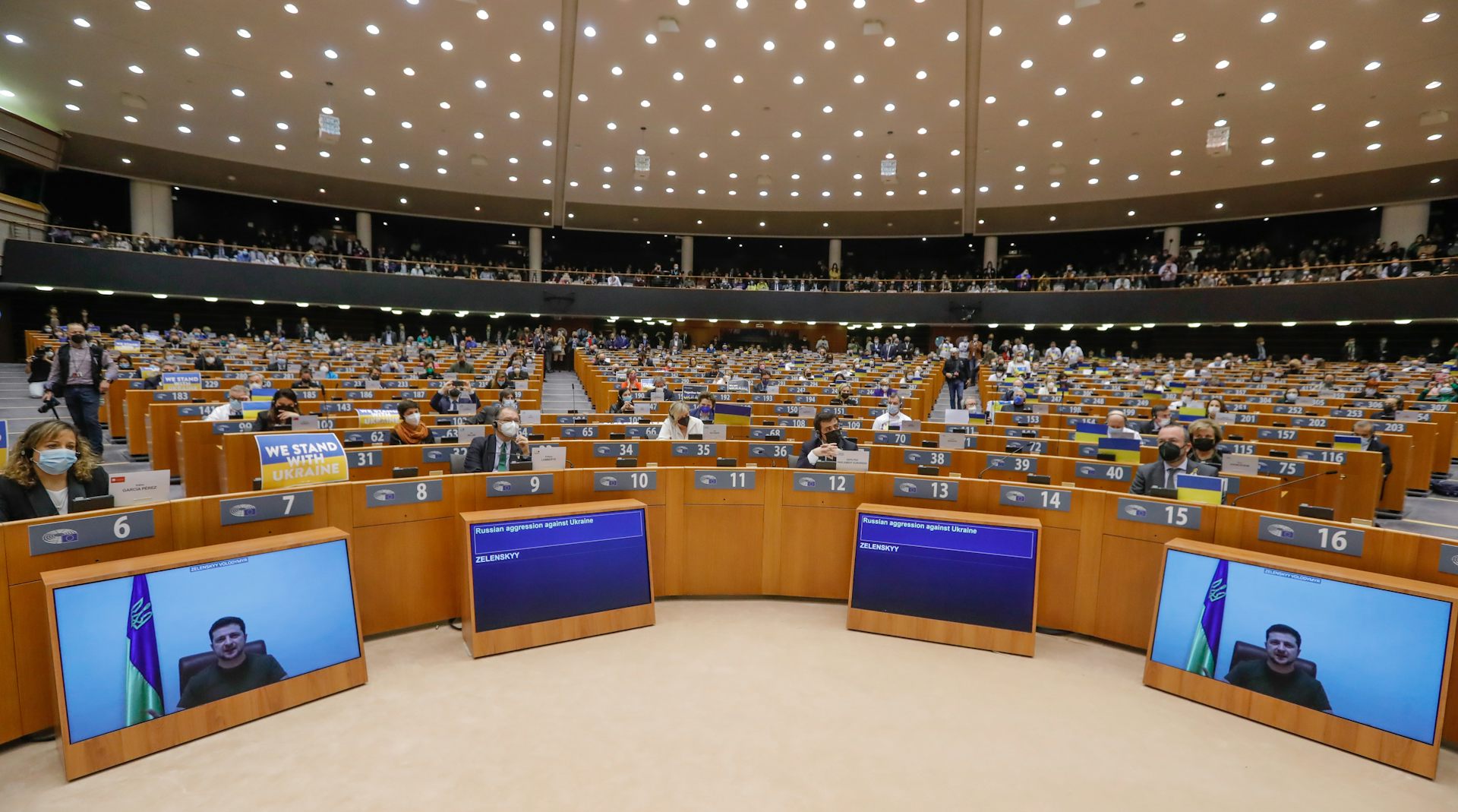 Ukranian president Volodymyr Zelensky appears on video screens in the chamber of the European Parliament while MEPs listen to his speech.