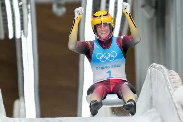 A woman sits on her luge with her arms raised cheering