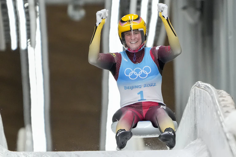 A woman sits on her luge with her arms raised cheering
