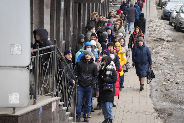 A long line of people wait outside of a bank.