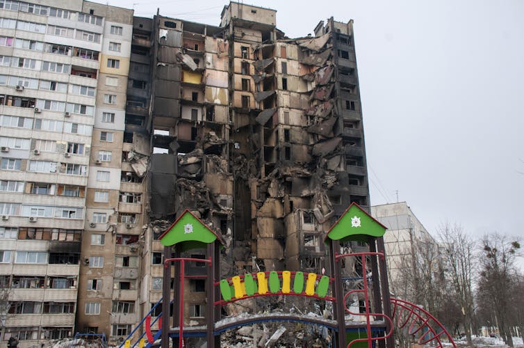 the burnt hull of an apartment building with a children's playground in the foreground