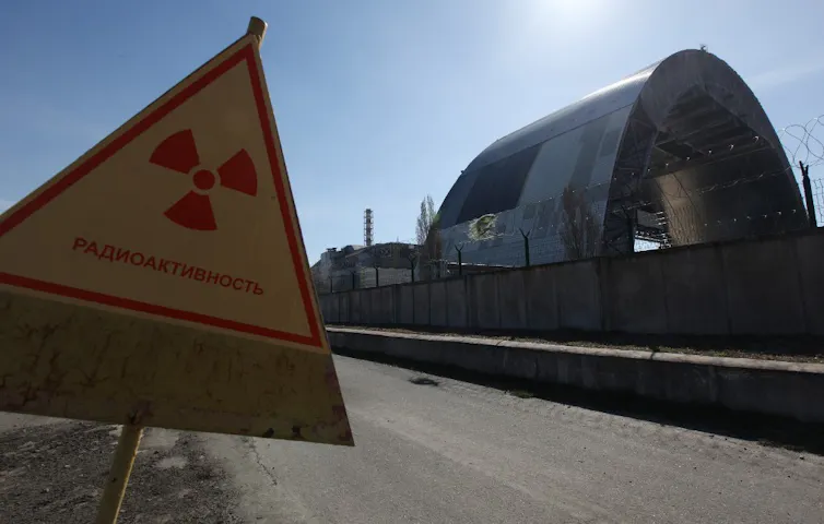 Vue du sarcophage en construction, avec un panneau d’alerte à la radioactivité en premier plan