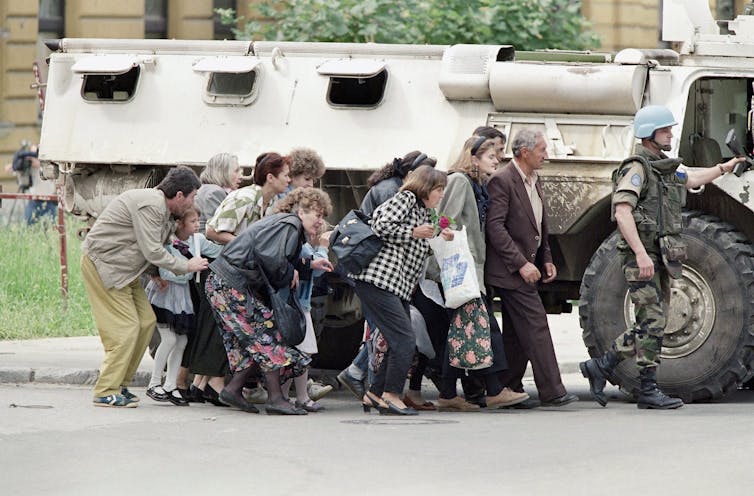 People crouched beside an armoured vehicle.