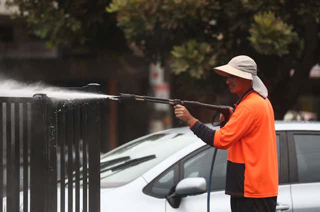 Man sprays fence while cleaning up after the floods.