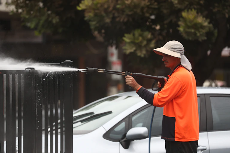 Man sprays fence while cleaning up after the floods.