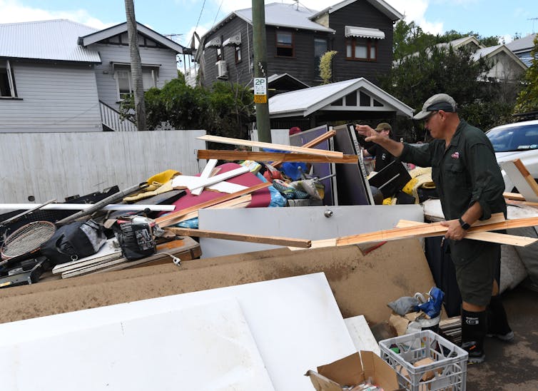 Man adds to a rubbish pile outside a flood-affected house.