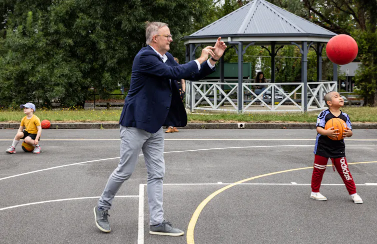 Man throws a basketball in a primary school yard.