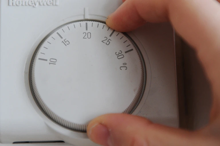 A hand turning the wheel on a thermostat.