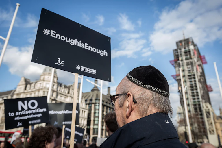 A man in a black yarmulke stands in the street surrounded by protest placards.