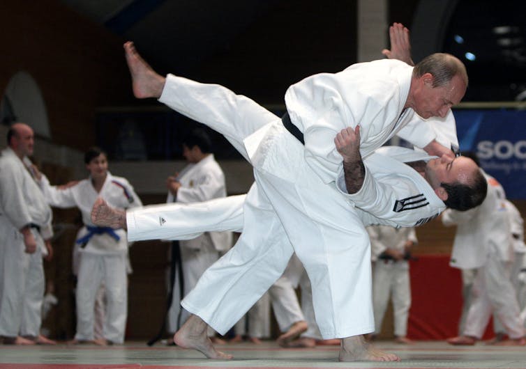 Two men in white judo costumes with one man throwing the other onto the floor.