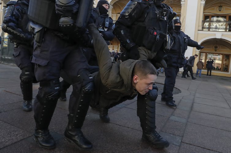 Hombre es llevado por la calle por varios policías.