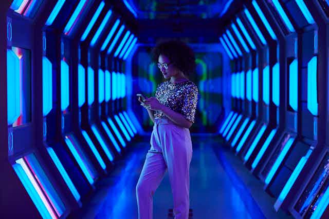 A woman stands in a high tech tunnel of lights, looking at her cellphone