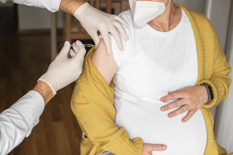 Pregnant woman wearing a mask and getting a shot.