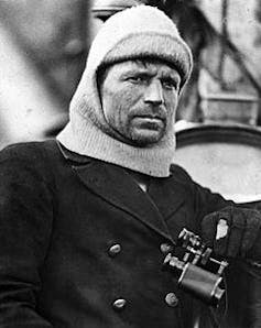 A man in a wool cap and wool coat, with binoculars hanging from his neck