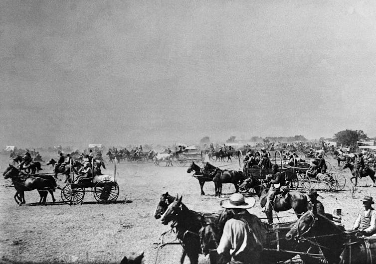 Horse-drawn carriages are scattered across a deep and flat landscape in a black and white photograph.