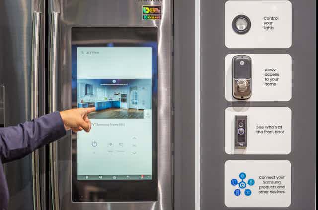 a hand points to a computer touchscreen embedded in the door of a refrigerator