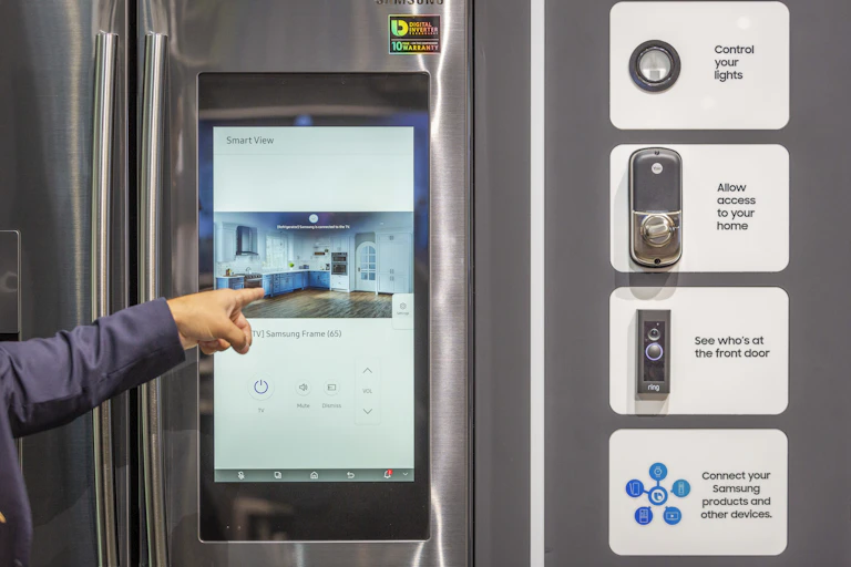 a hand points to a computer touchscreen embedded in the door of a refrigerator