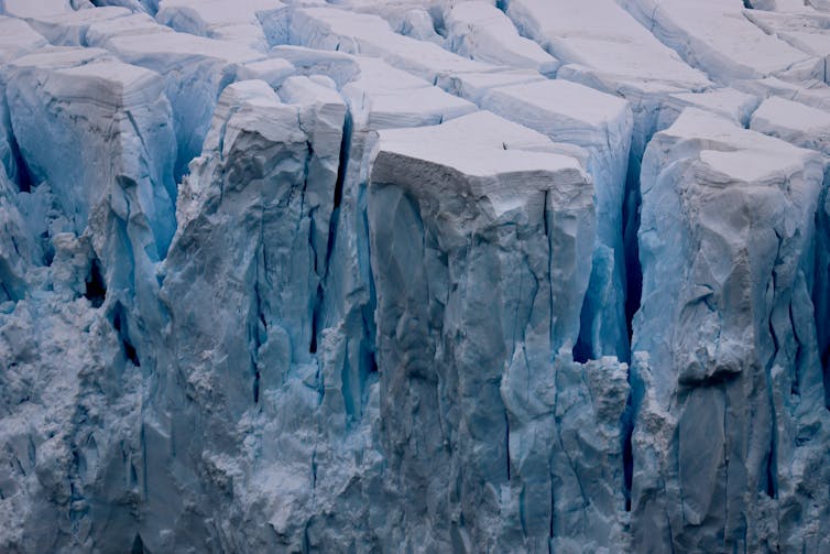 Deep cracks leaves jagged columns of ice with a layer of snow at the top ready to tip into the sea.