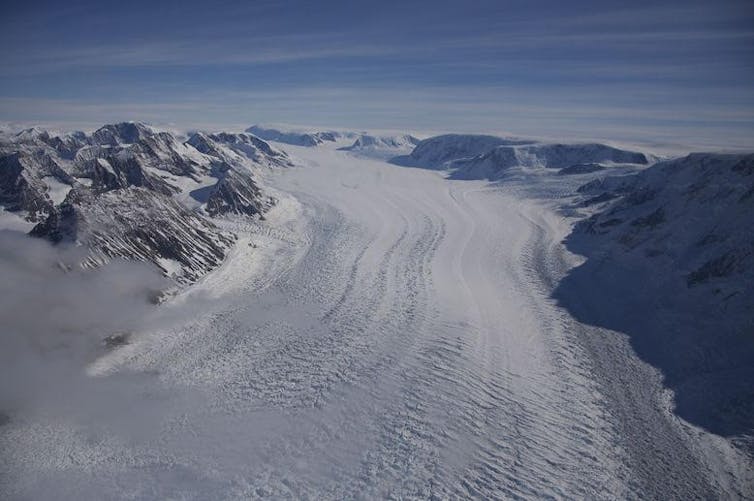 An Antarctic glacier flows between mountains. Lines in ice show that it's flowing.