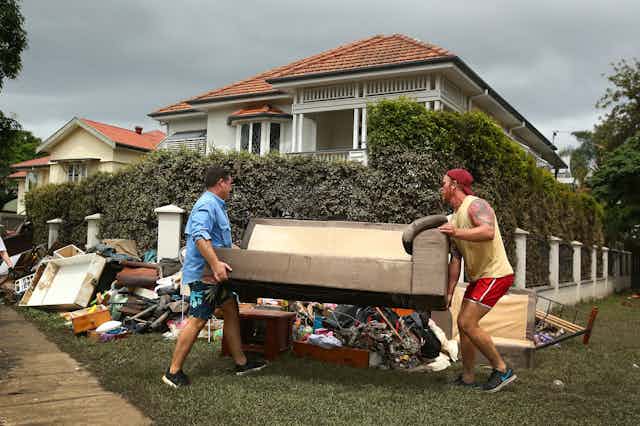 two men carry furniture to pile