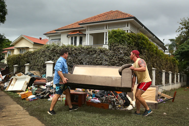 two men carry furniture to pile