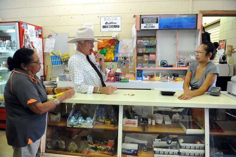 man in hat stands behind counter with two women
