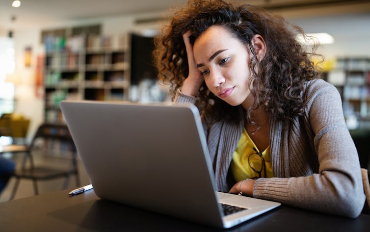 ADHD looks different in adults. Here are 4 signs to watch for. Women with dark curly hair looking frustrated as she looks at her laptop. 