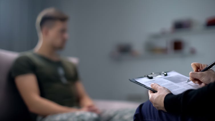 Man sits while a clinicians ticks off list on clipboard