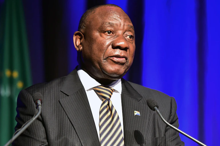 A man wearning a shirt, jacket and tie speaks into two small microphones at a podium.
