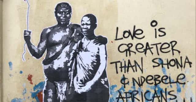 A street art murall showing a man in traditional attire with his arm around a woman, also in traditional attire. He holds a string with a red balloon at the end of it. Next to them the words 'Love is greater than Shona & Ndebele Africans.