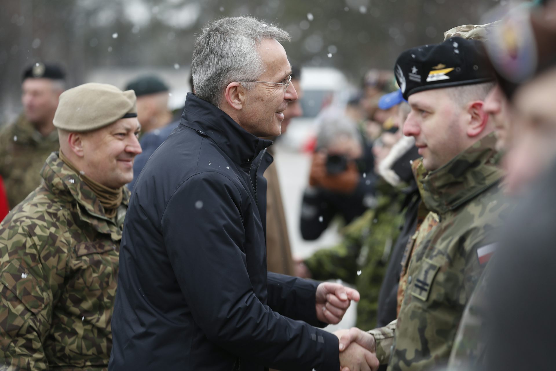 Man shakes hands with uniformed soldiers in snow.