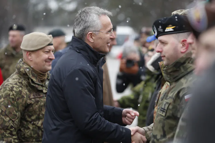 Man shakes hands with uniformed soldiers in snow.