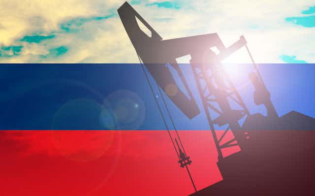 Silhouette of oil drill on Russian flag backdrop.