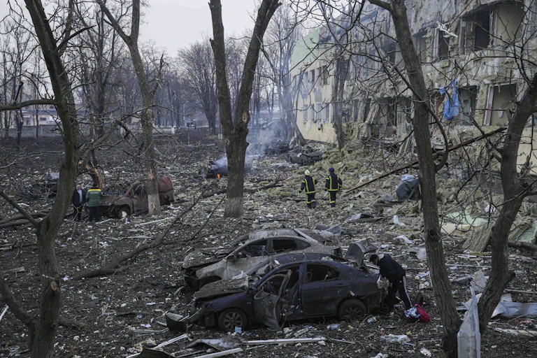 Emergency workers walk among the smoky ruins of a building and burnt cars and trees