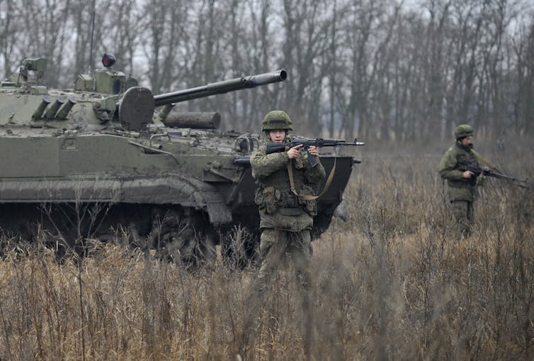 A tank and soldier holding guns in a field.