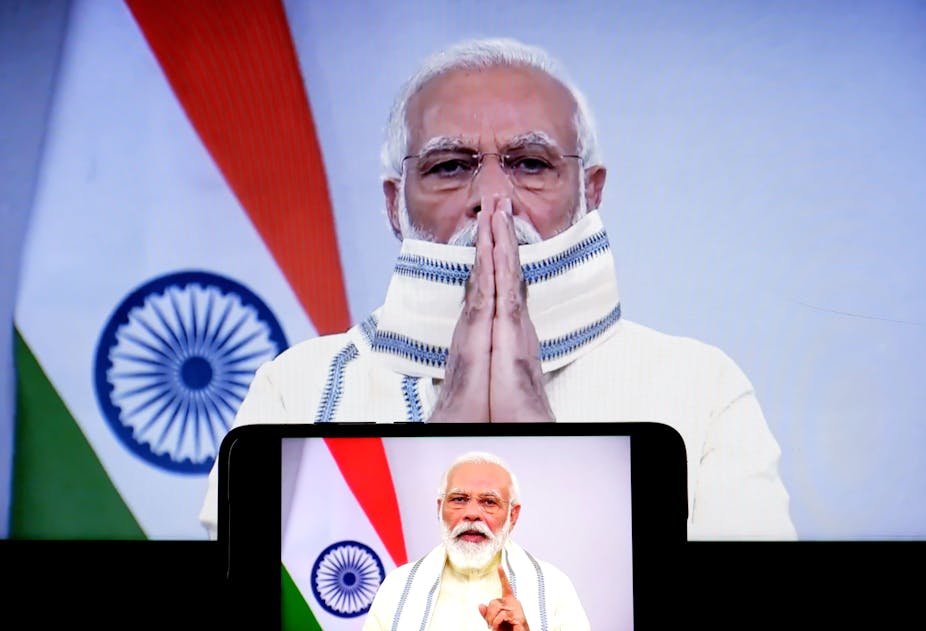 Prime Minister Narendra Modi stands in front of the Indian flag hands pressed together.