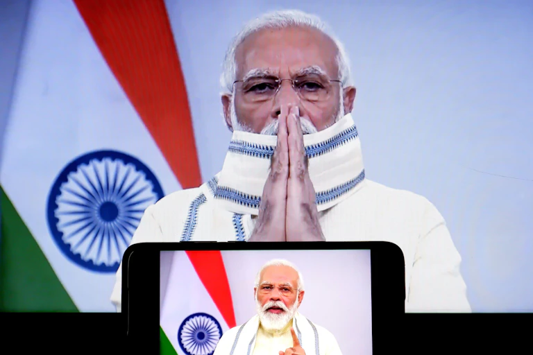 Prime Minister Narendra Modi stands in front of the Indian flag hands pressed together.