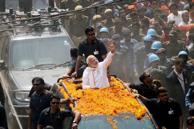 Prime Minister Modi waving from a car driving down a busy street.